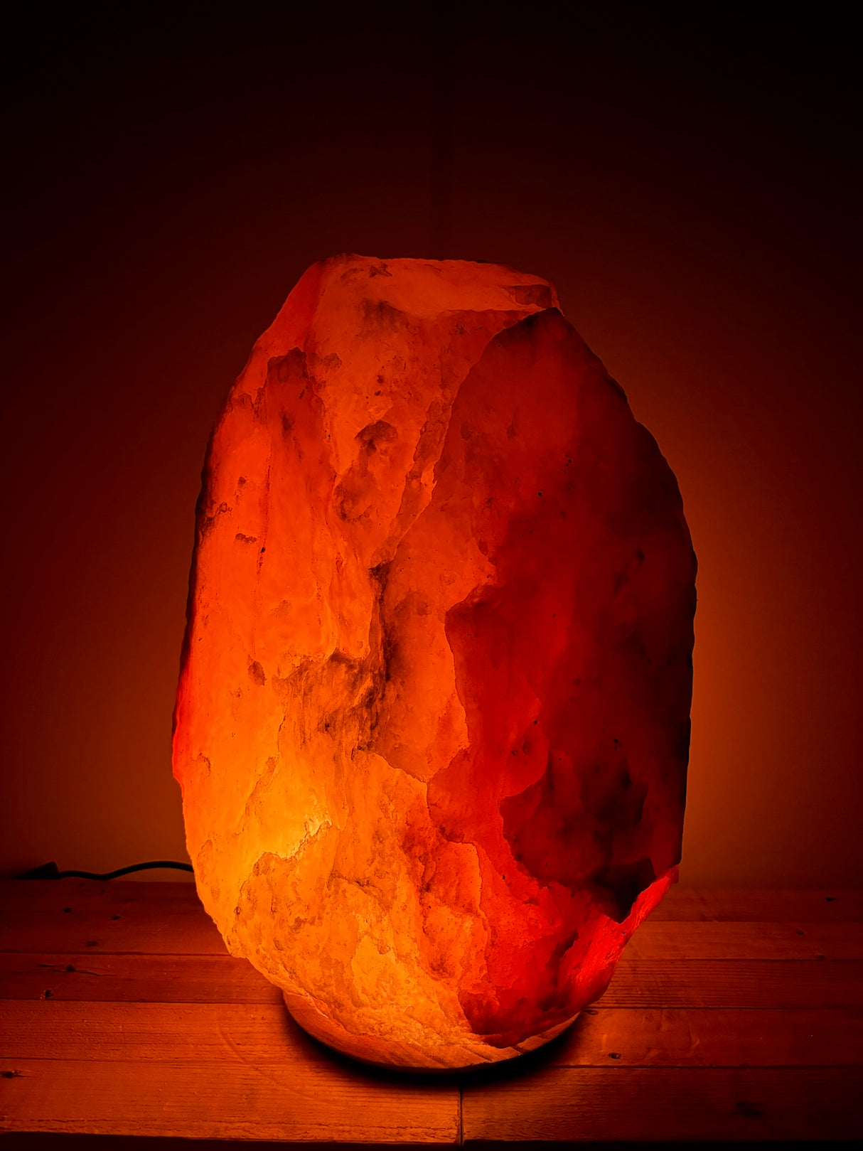 Donkere Himalaya zoutlamp 45–50 kg met warme rood/oranje gloed op stevige houten voet