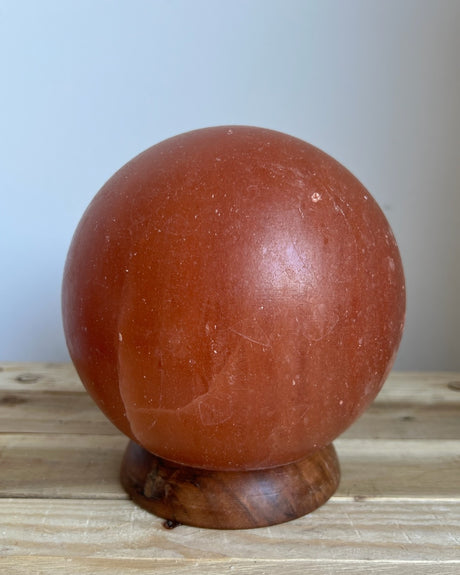 Handgemaakte bolvormige Himalaya zoutlamp van 4 kg op houten voet, verspreidt warm licht en draagt bij aan een rustgevende sfeer en natuurlijke luchtzuivering.
