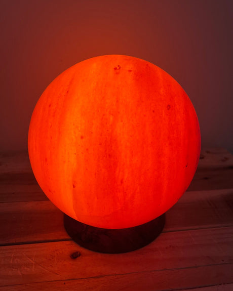 Handgemaakte bolvormige Himalaya zoutlamp van 4 kg op houten voet, verspreidt warm licht en draagt bij aan een rustgevende sfeer en natuurlijke luchtzuivering.