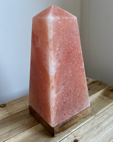 Handgemaakte Himalaya zoutlamp in obeliskvorm van 3 kg op houten voet, straalt warm licht uit en ondersteunt een ontspannen sfeer en natuurlijke luchtzuivering.