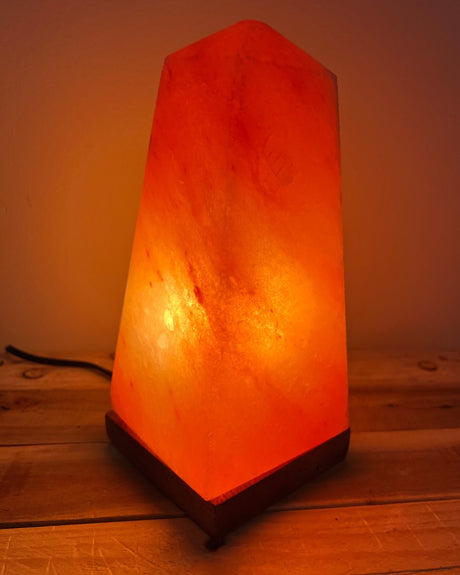 Handgemaakte Himalaya zoutlamp in obeliskvorm van 3 kg op houten voet, straalt warm licht uit en ondersteunt een ontspannen sfeer en natuurlijke luchtzuivering.