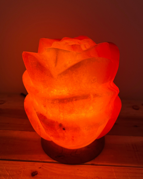 Lotus-vormige Himalaya zoutlamp op houten voet, rustgevend licht en symboliek van zuiverheid en groei.