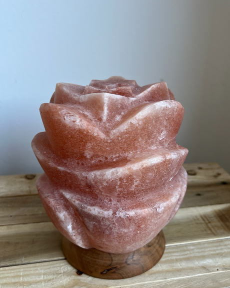 Lotus-vormige Himalaya zoutlamp op houten voet, rustgevend licht en symboliek van zuiverheid en groei.