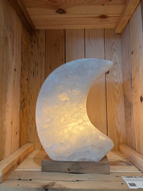 Maanvormige Himalaya Zoutlamp in roze, grijs en wit met warme gloed en houten voet.