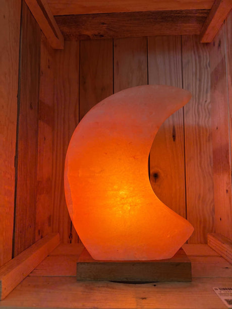 Maanvormige Himalaya zoutlamp in roze, grijs en wit met zachte gloed en houten voet.