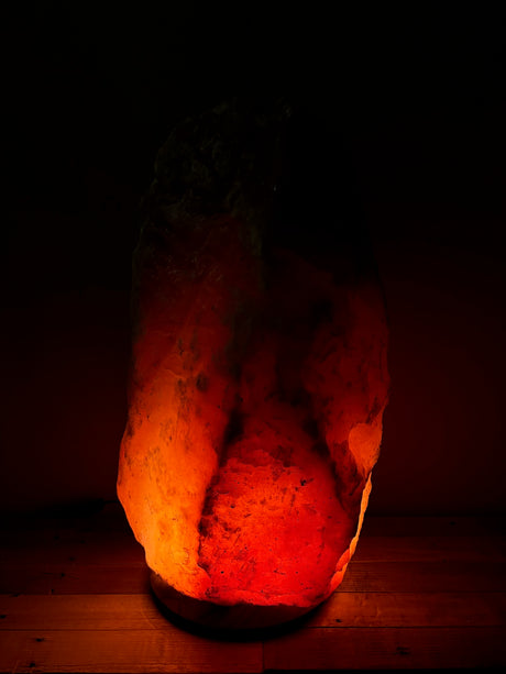 Donkere Himalaya zoutlamp 50–60 kg met diepe rood/oranje gloed op stevige houten voet